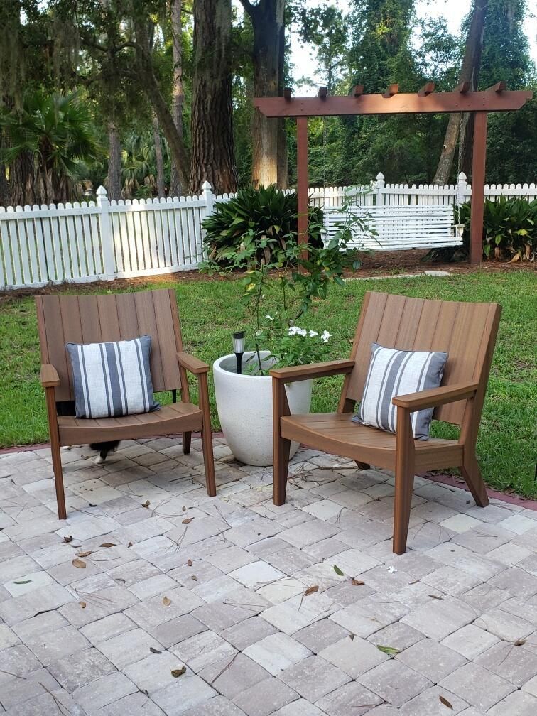 Patio seating area with two wooden chairs, striped pillows, a small table, and a garden backdrop