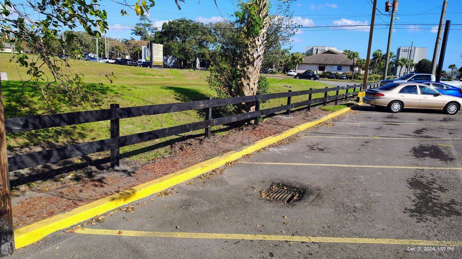 A car is parked in a parking lot next to a wooden fence.