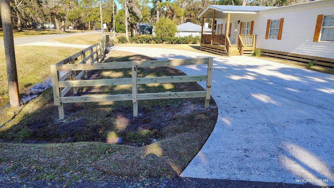 A wooden fence is surrounding a gravel driveway in front of a mobile home.