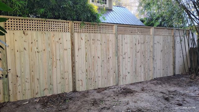 A wooden fence with a lattice top is sitting in the dirt in front of a house.