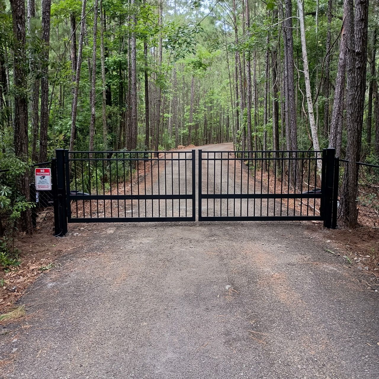 Black metal gate on a gravel road leading into a forest. A
