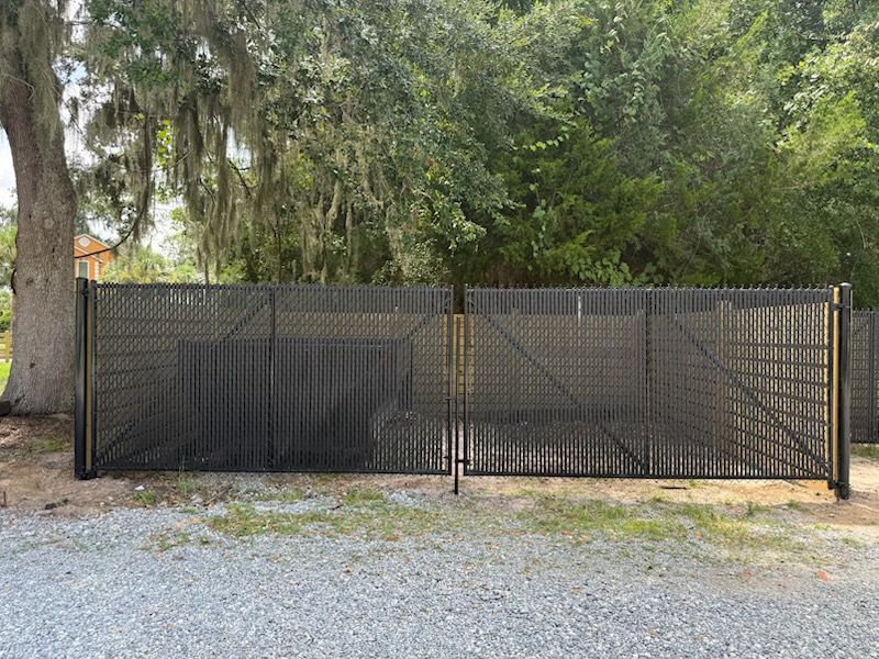Black metal gate with a lattice design, set on a gravel driveway, with trees in the background.