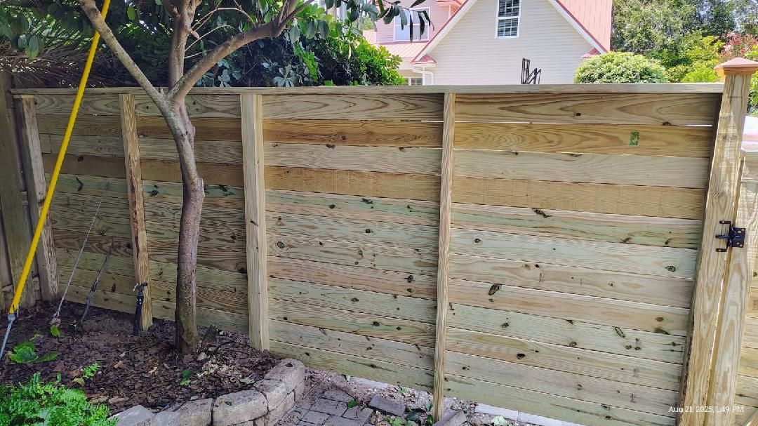 Wooden fence with horizontal planks, framing a yard, with a tree growing through it.