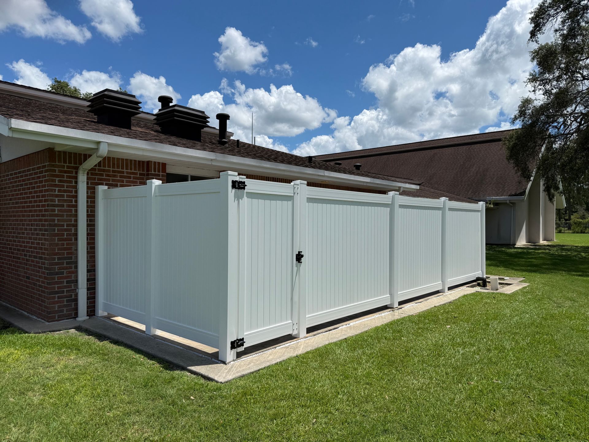 White vinyl fence enclosure next to a brick building, under a blue sky with clouds.