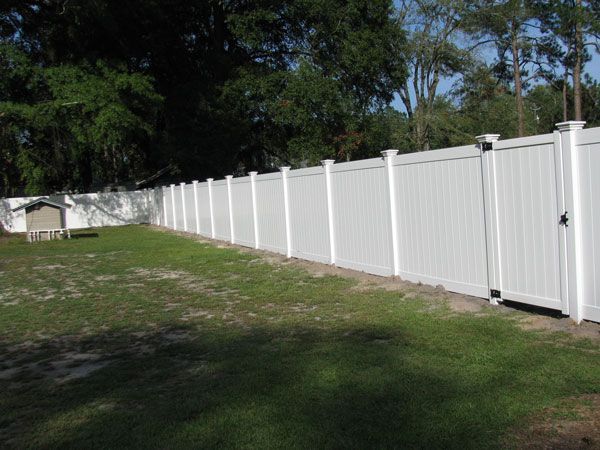 White vinyl fence surrounding a grassy yard, with trees in the background and a small shed on the left.