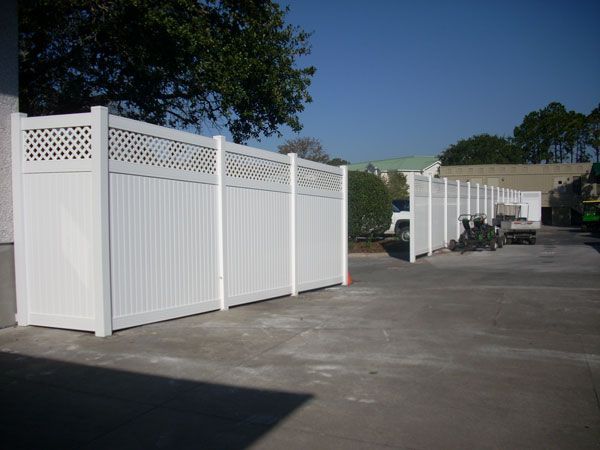 White vinyl fence with lattice top section in an outdoor parking lot. The fence runs along the edge of the lot.