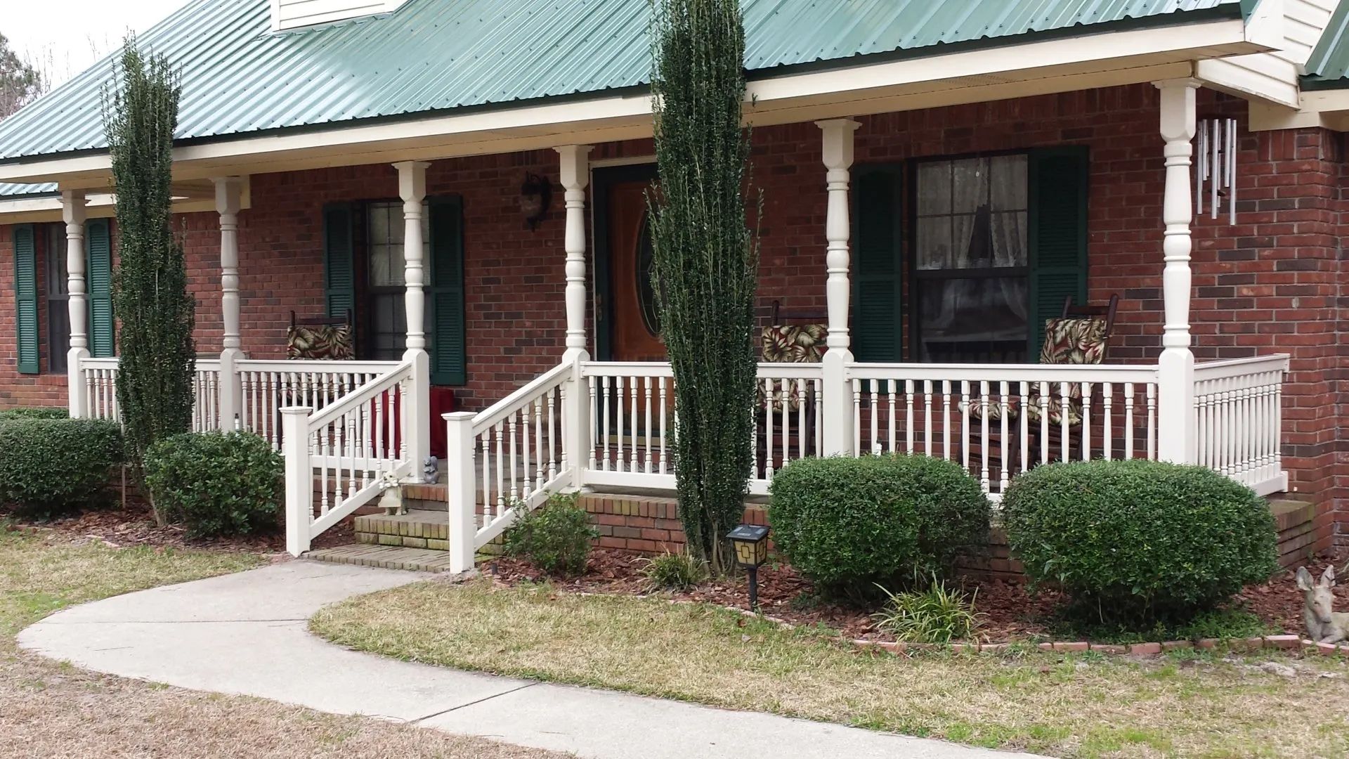 a brick house with a green roof and a white porch