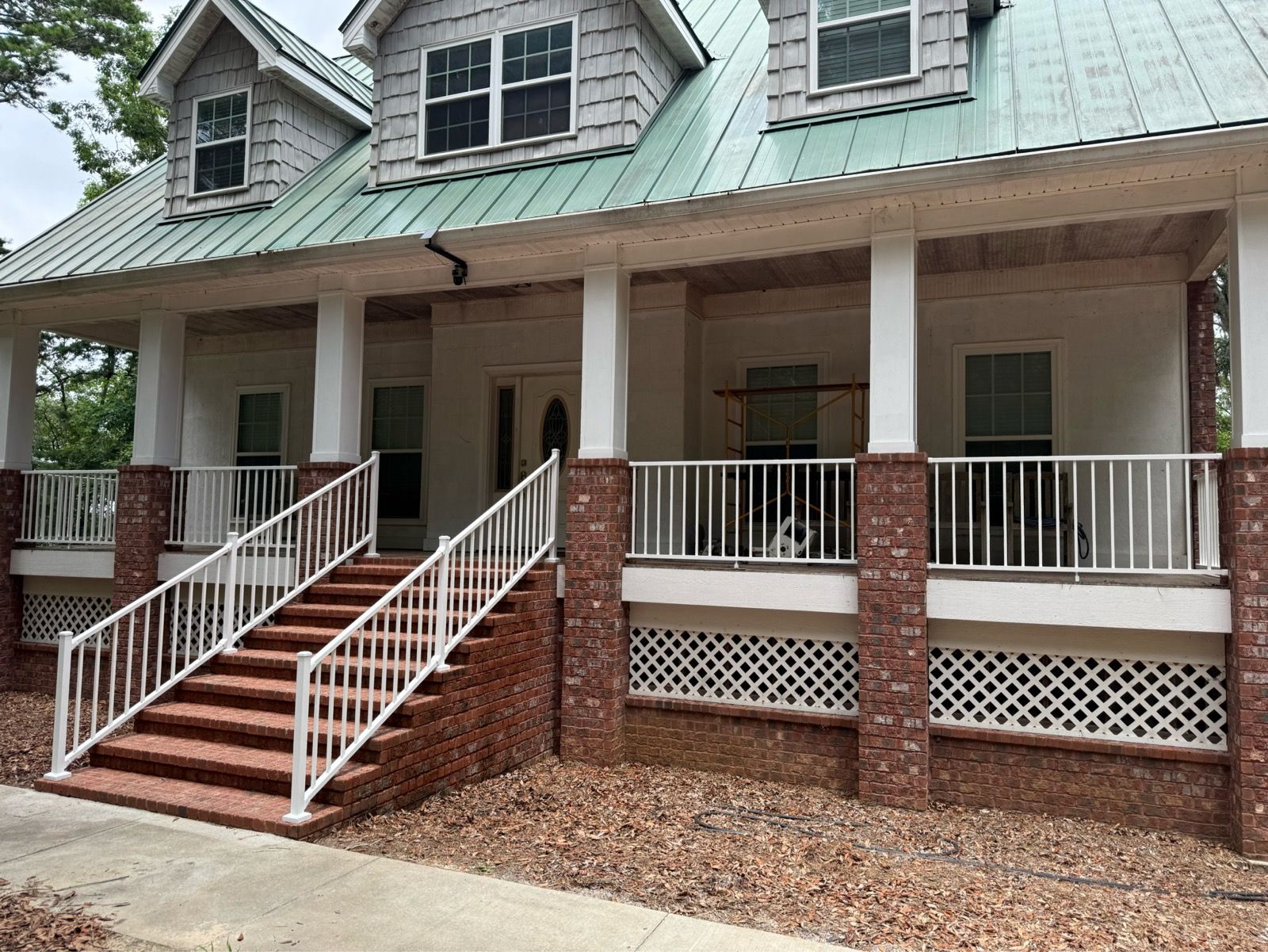 Front porch of a brick house with white railings, green metal roof, and steps leading up to the entrance