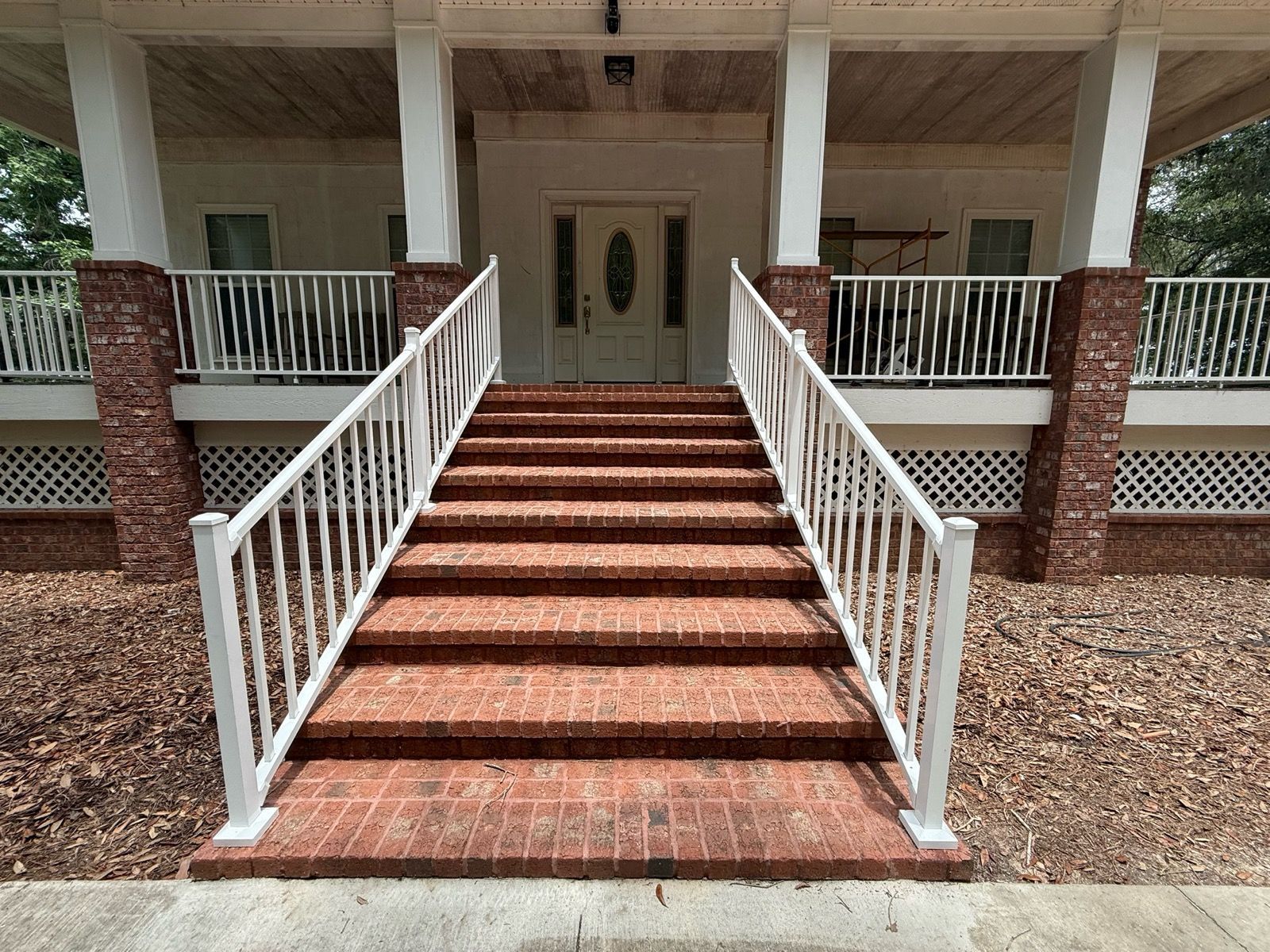 Front steps of a house with red brick stairs, white railings, and a covered porch.
