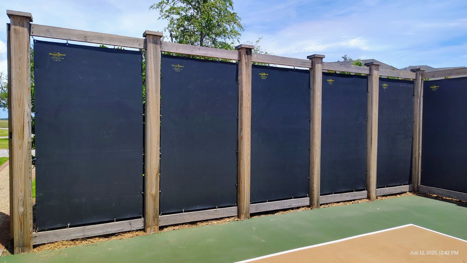 Black privacy screens attached to wooden posts in an outdoor recreational area.