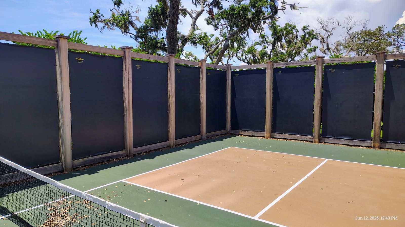 A pickleball court with a dark privacy fence and net, green and tan colors.