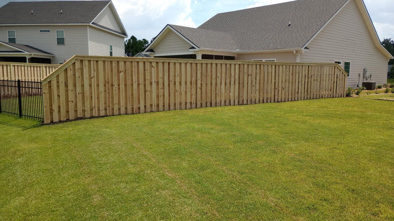Wooden privacy fence along a grassy backyard beside suburban houses under a cloudy sky