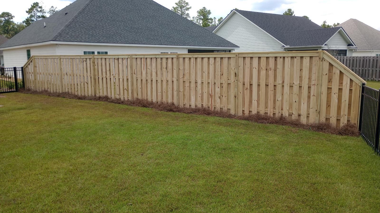 Backyard with a long wooden privacy fence and green lawn, with houses visible behind it