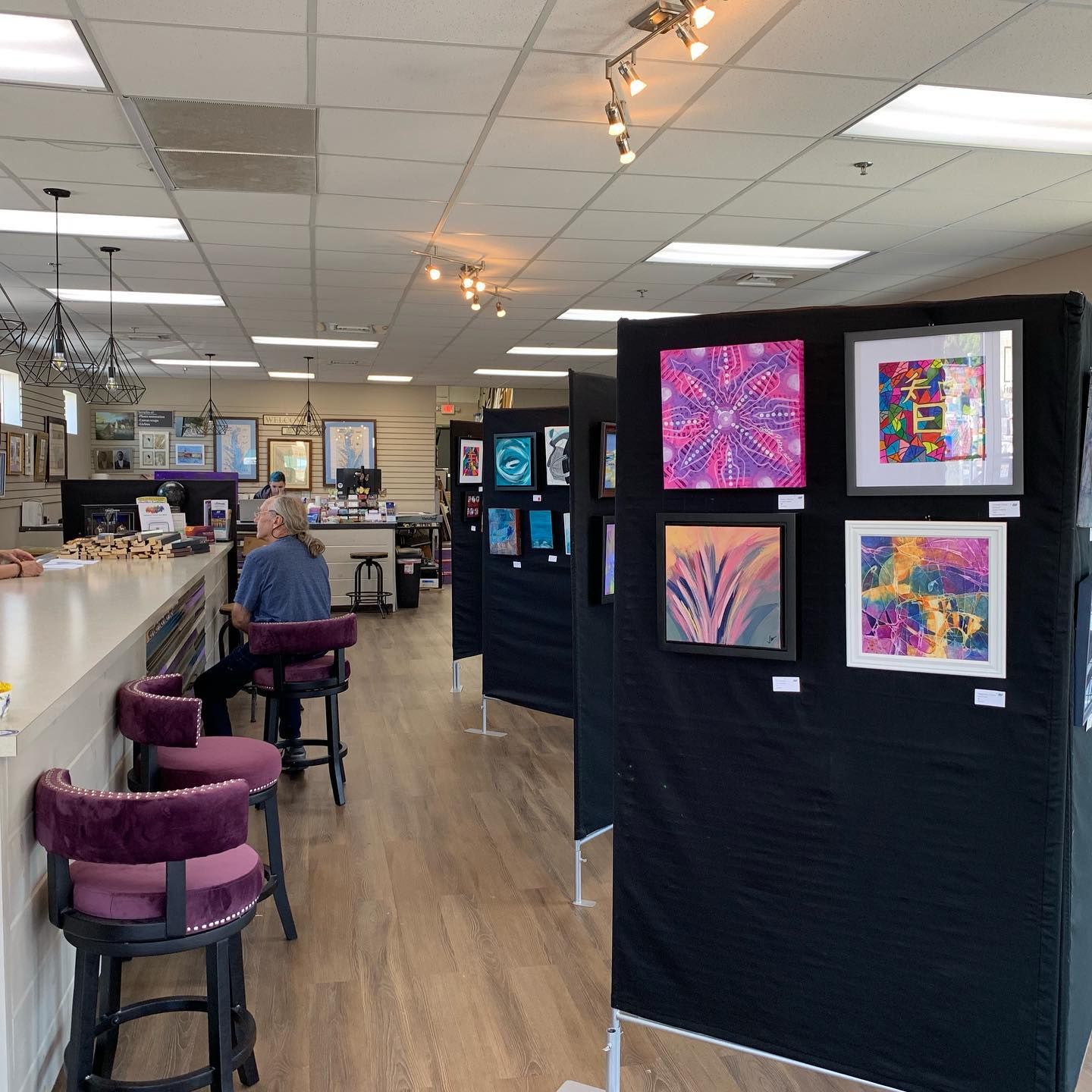 Art gallery with colorful abstract paintings displayed on black partitions in a bright café-like room