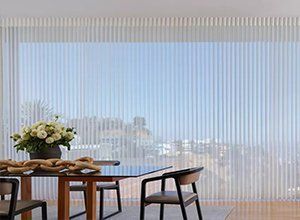 A dining room with a table and chairs and vertical blinds.