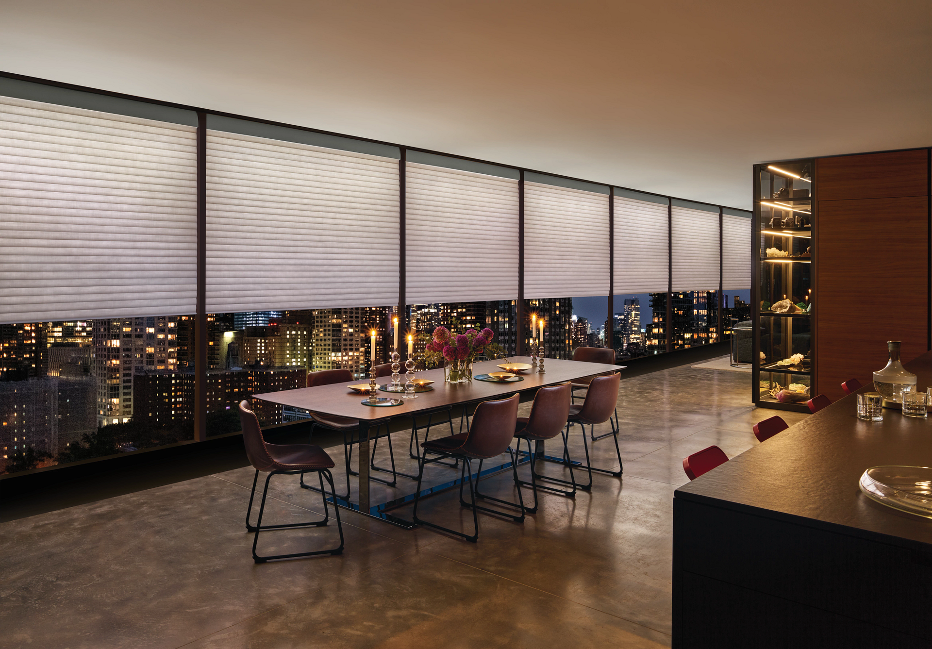 A dining room with a long table and chairs and a view of the city at night.