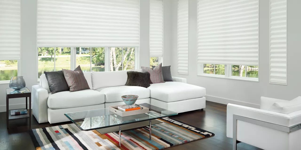 A living room with a white couch, chair, coffee table, and striped blinds.