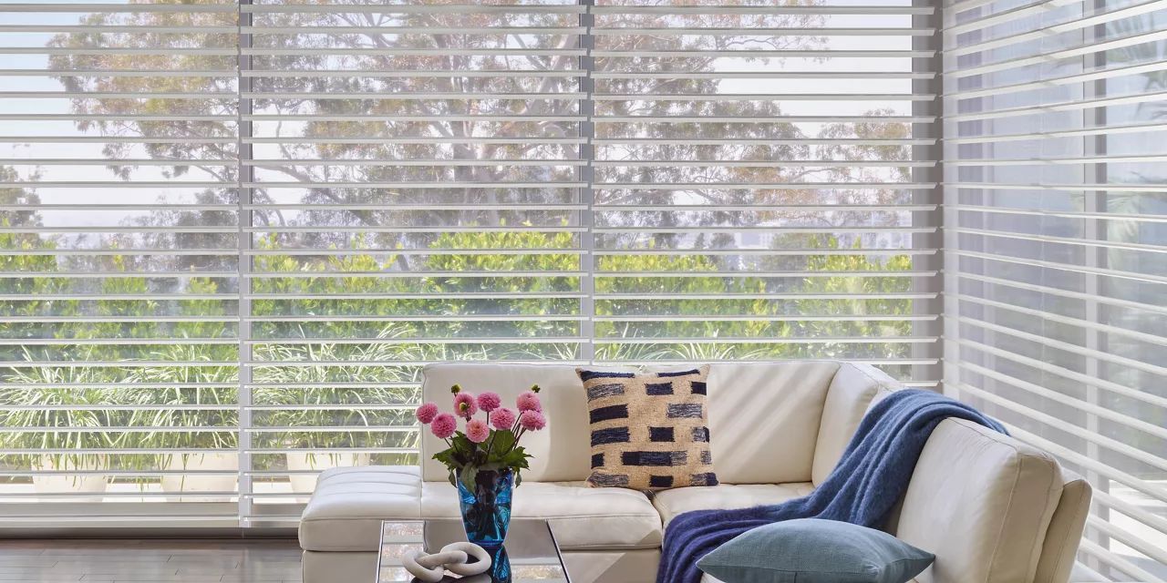 A living room with a couch , table , vase of flowers and blinds.