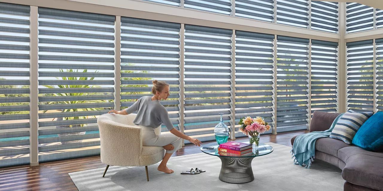 A woman is sitting in a chair in front of a window in a living room.