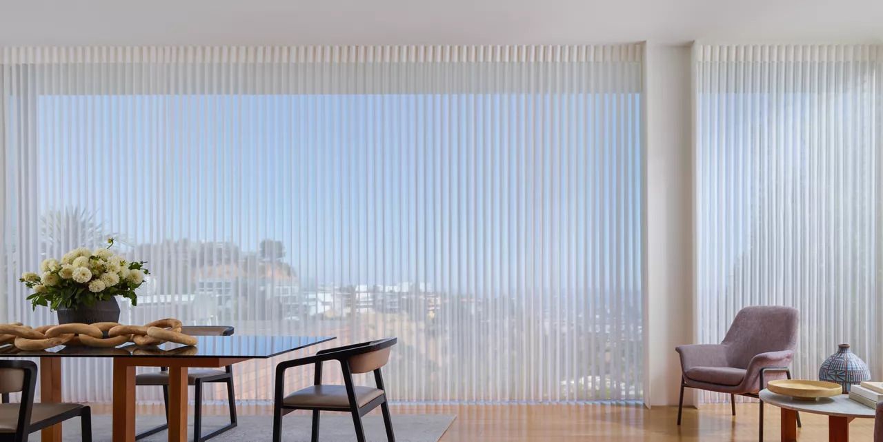 A living room with a table and chairs and vertical blinds on the windows.