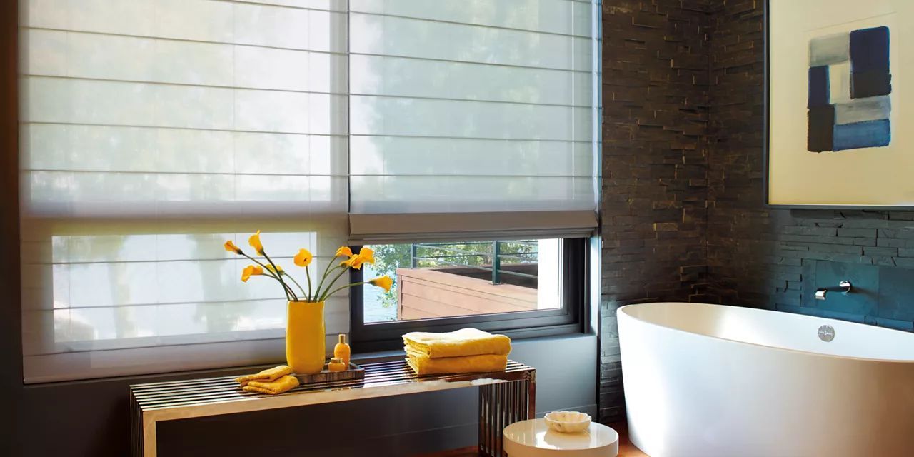 A bathroom with a tub and a window with Roman shades.