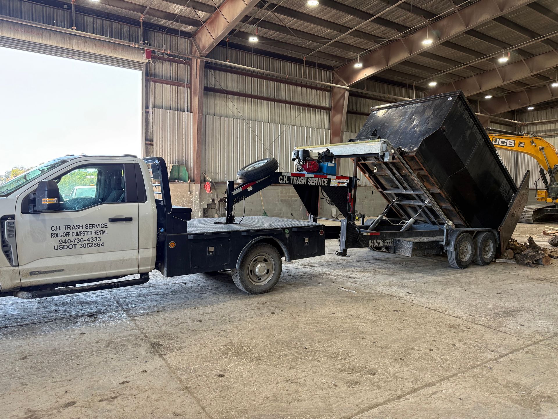 Truck with attached dump trailer inside a large industrial building, unloading debris.