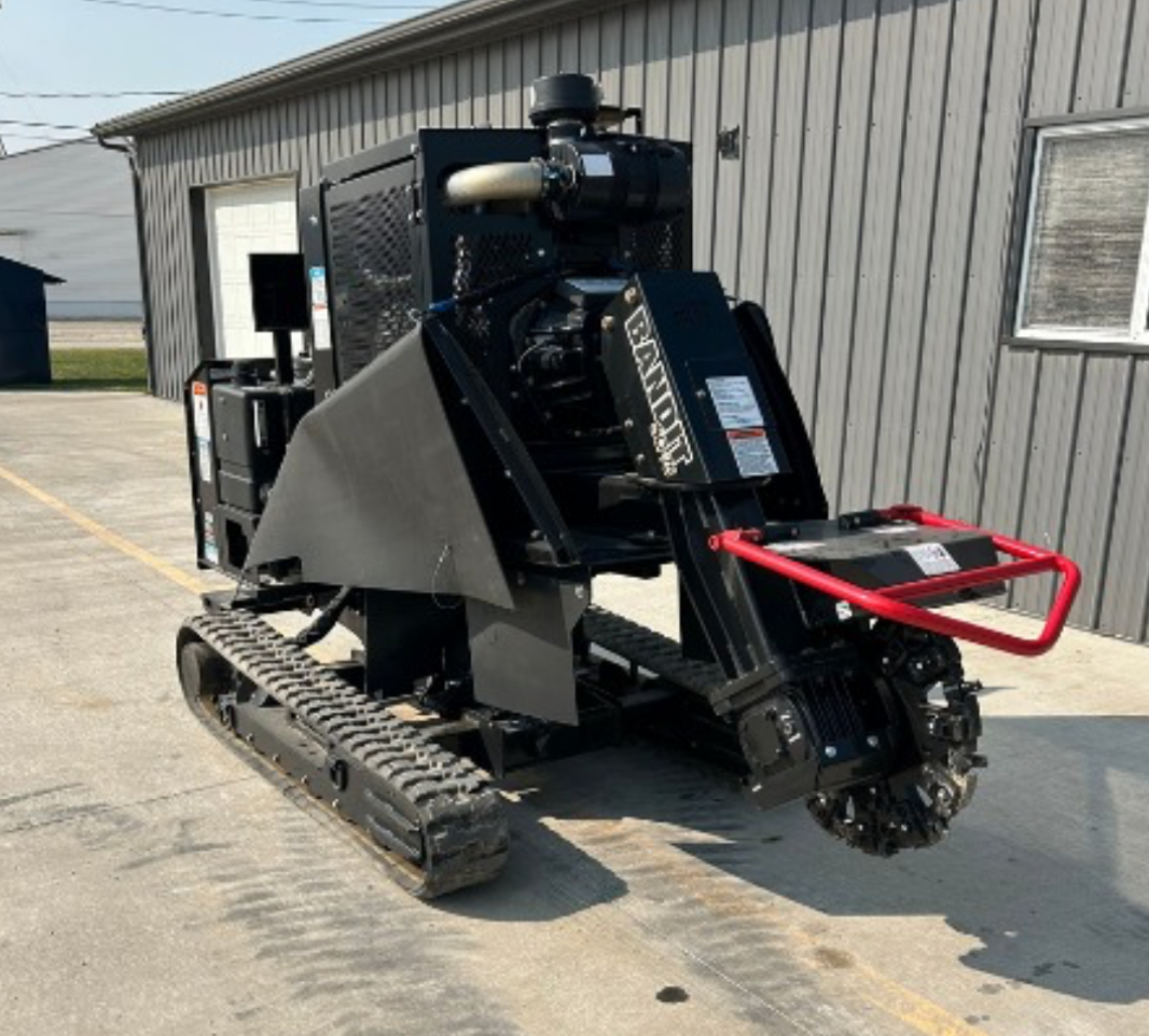 A stump grinding machine with a red handle is parked in front of a building