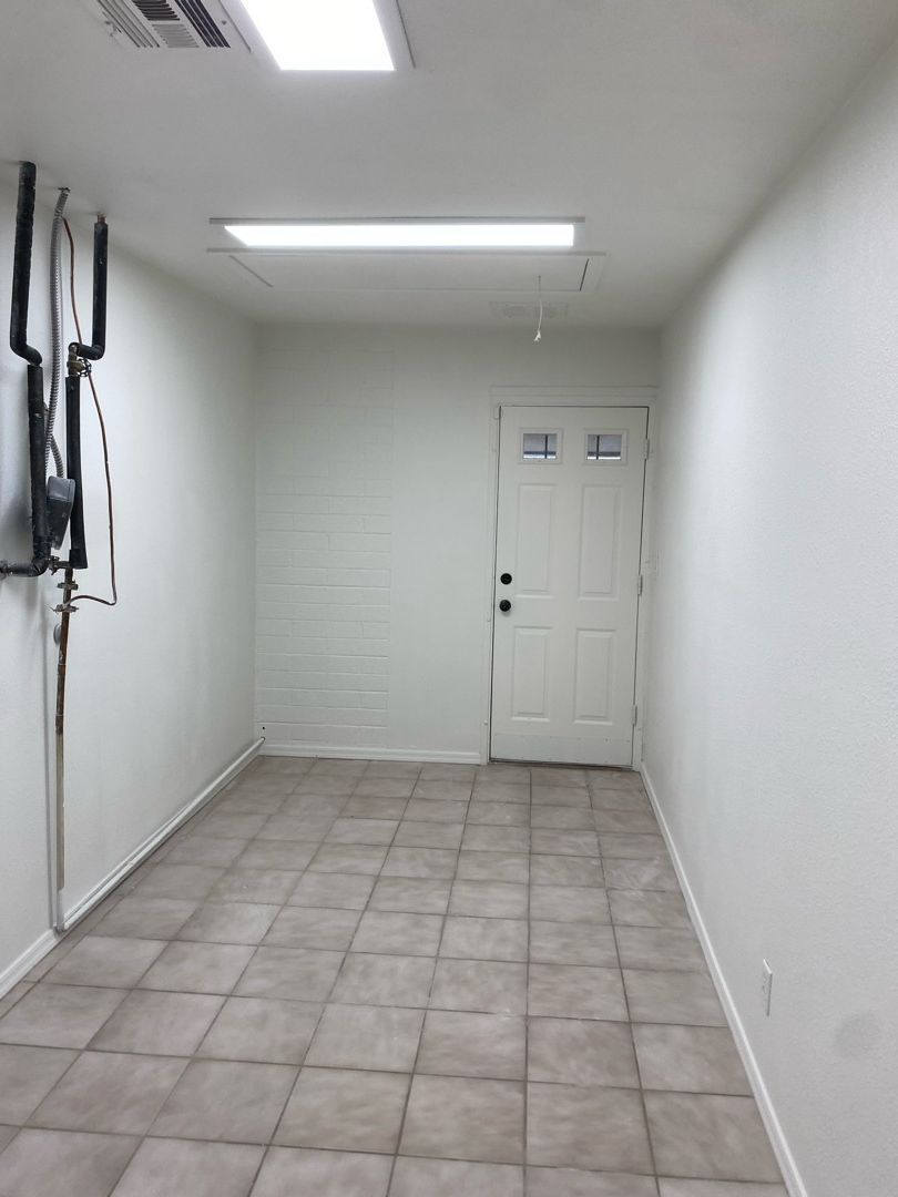 A long hallway with tile floors and white walls leading to a door.