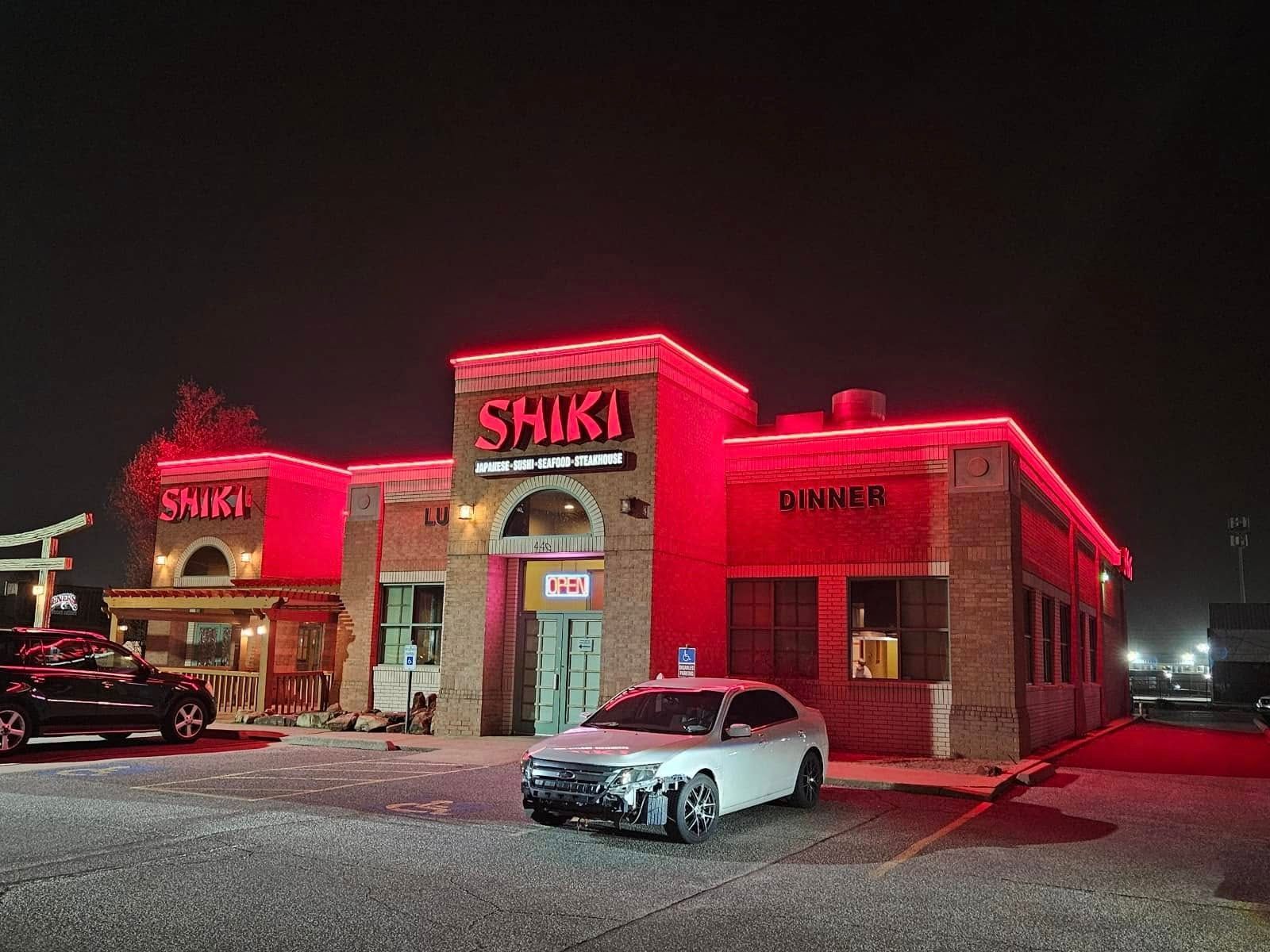 A car is parked in front of a shiki restaurant at night.