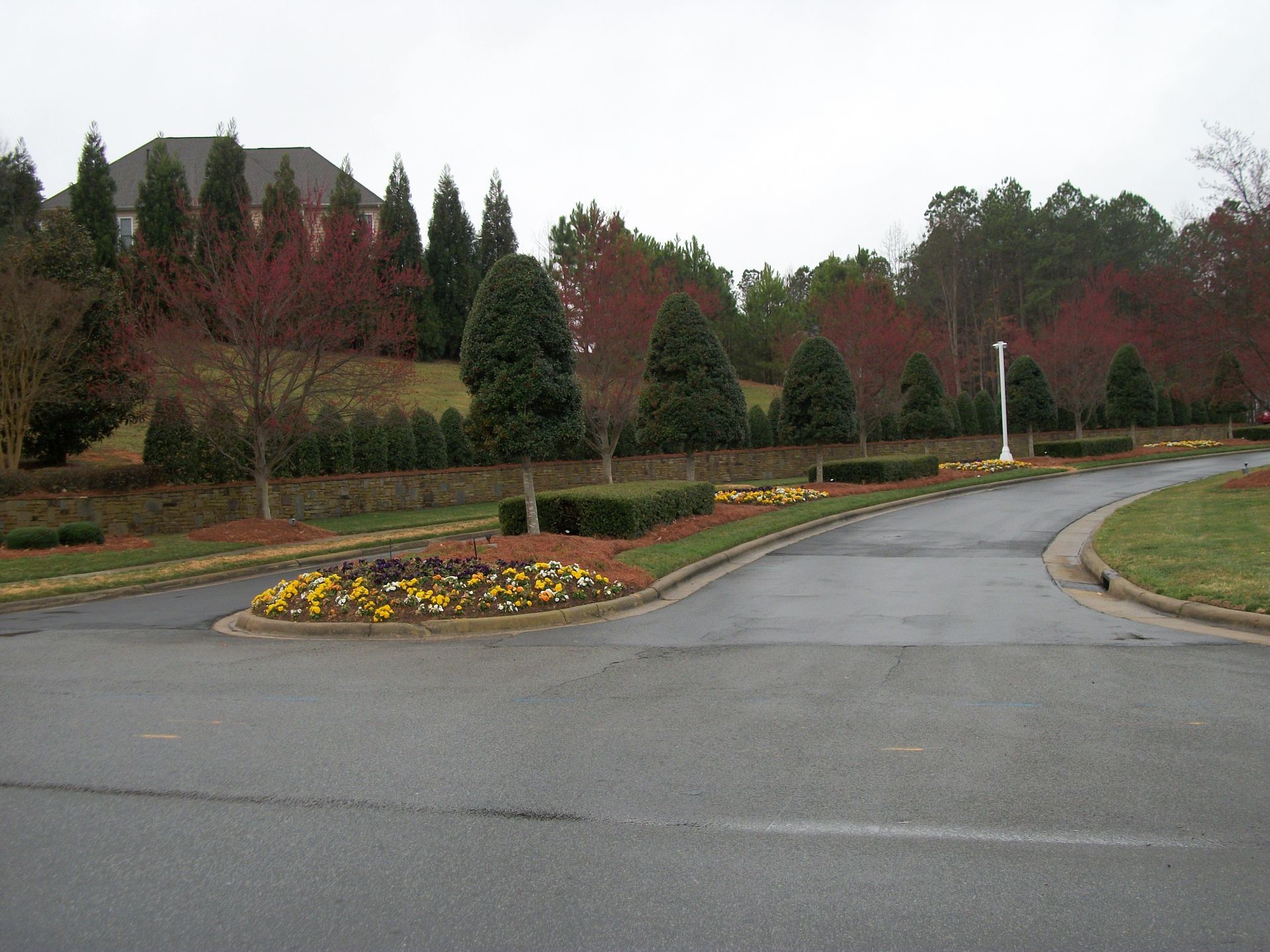 Curving driveway through a landscaped campus with flower beds, trees, and a building in the background
