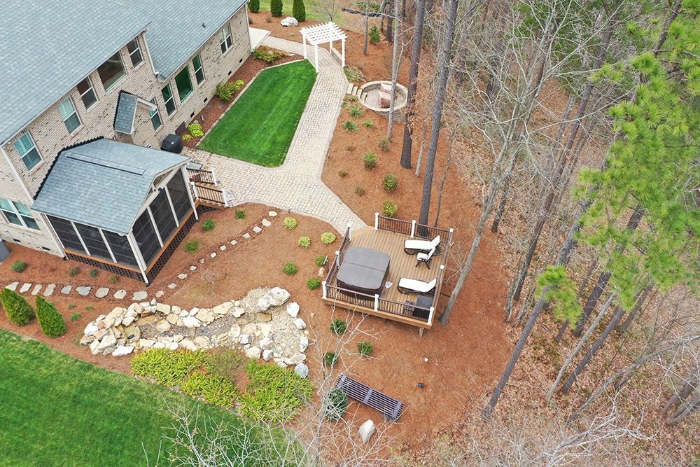Aerial view of a backyard patio with seating, stone path, and fire pit beside a house and trees