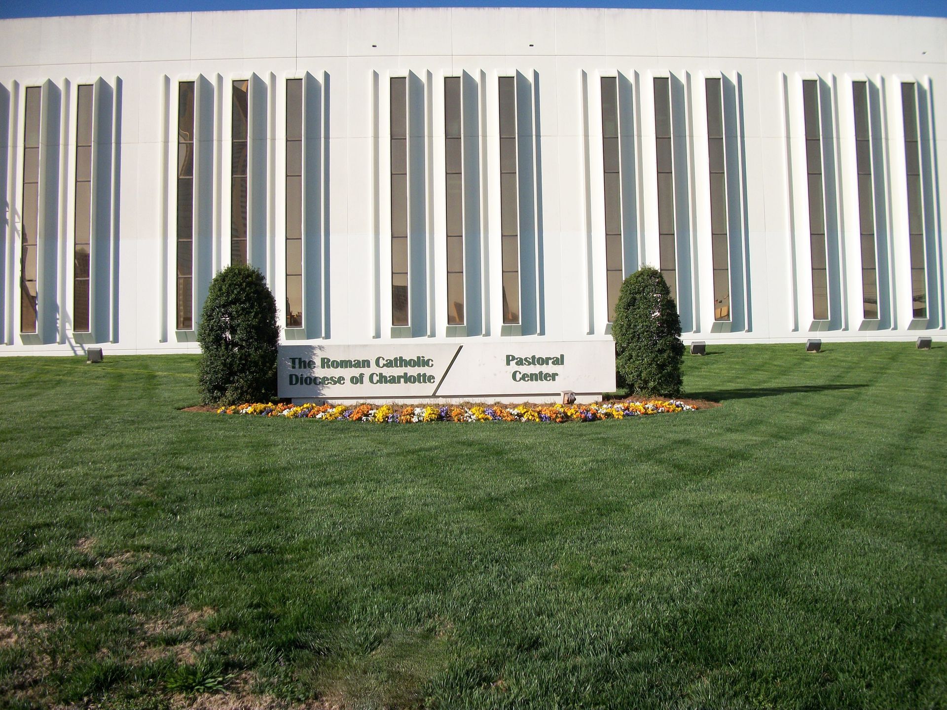 Brianna Carmel Library sign in front of a white building and green lawn with flowerbed and shrubs