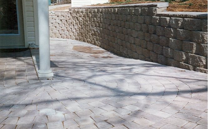 Curved stone patio beside a white column and retaining wall, with a doorway on the left.