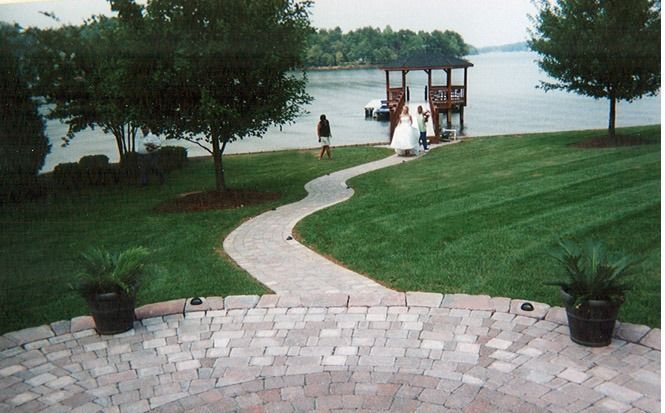 Wedding couple by a lakeside gazebo, with a winding stone path and manicured green lawn