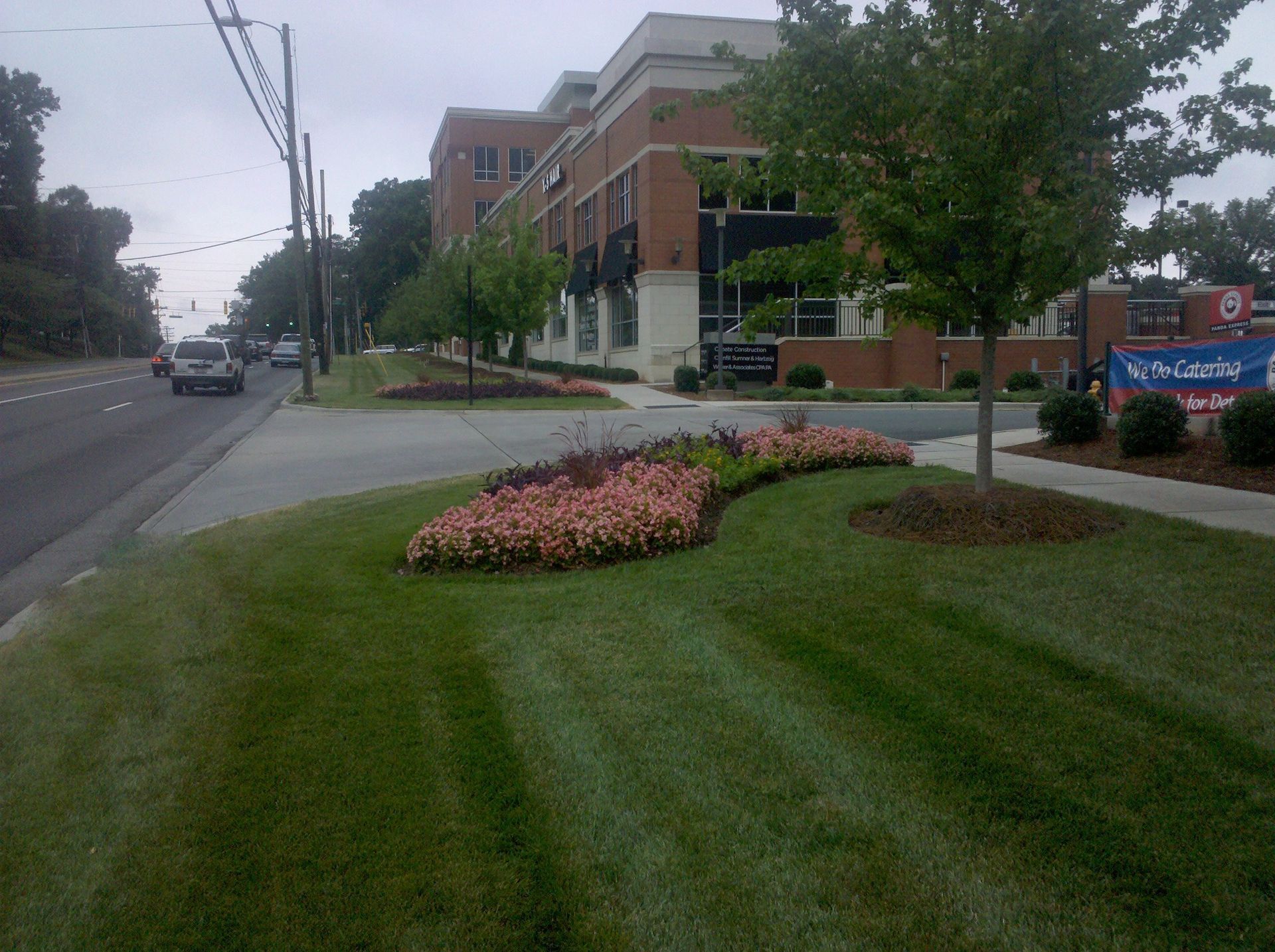 Brick office building beside a road, with manicured grass and pink flower beds under cloudy skies
