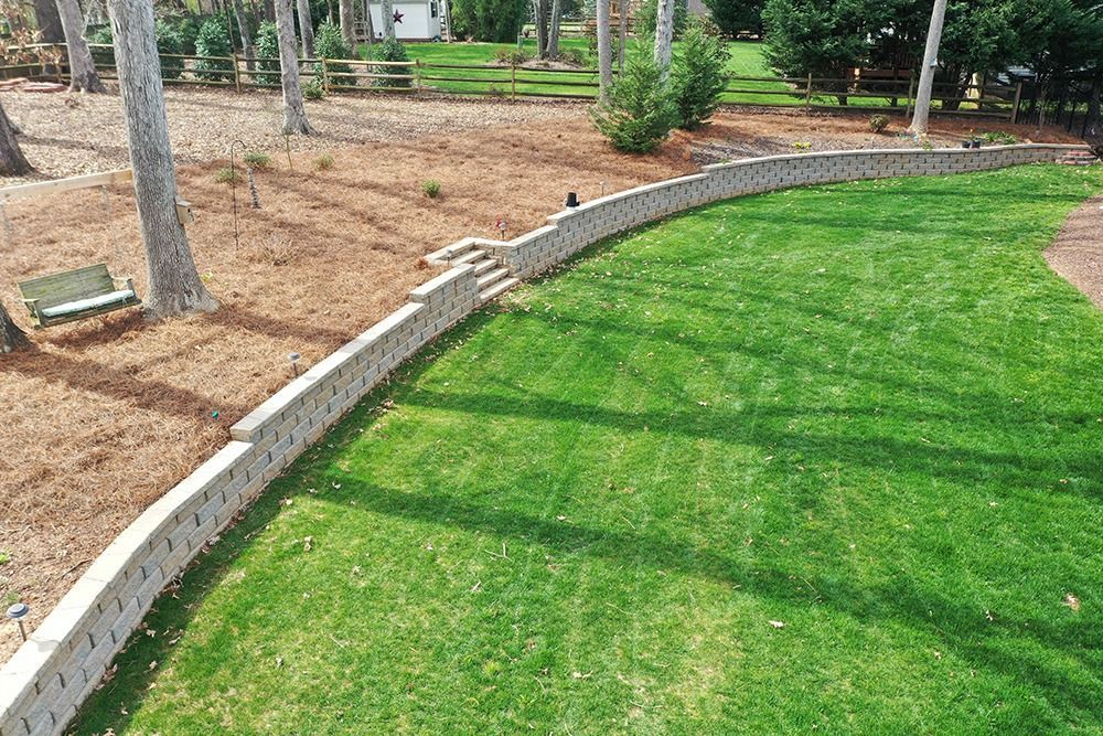 Curved stone border separating green lawn from a mulched garden bed with trees and shrubs