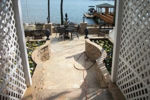 Stone walkway with white lattice arches leading to a seaside patio with tables and ocean view