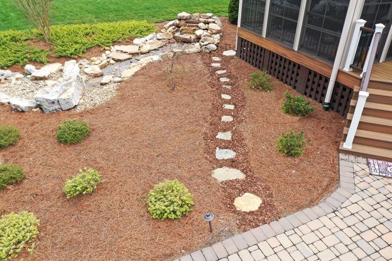 Xeriscaped garden bed with stepping stones, white rocks, and small shrubs beside a house deck