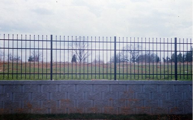 Iron fence atop a stone wall overlooking a grassy field under a cloudy sky