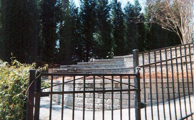 Black metal fence before stone steps and retaining wall in a wooded outdoor area