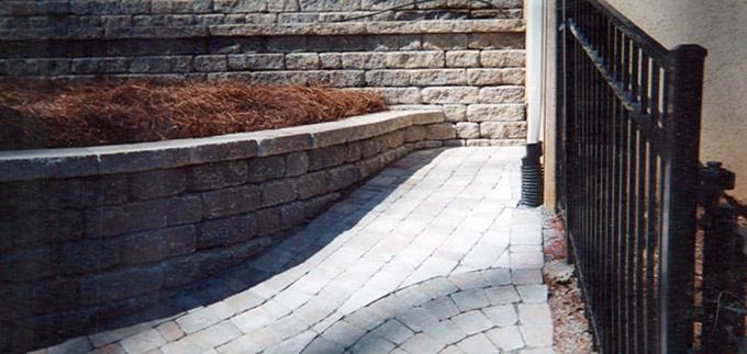 Curved stone walkway beside a low stone wall and black metal fence in sunlight