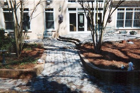 Courtyard walkway with bare trees, brick planters, and a building entrance in the background