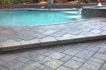 Poolside stone patio beside turquoise water and a low waterfall