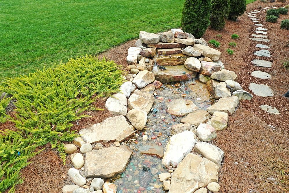 Small stone-lined garden stream with stepping stones and green grass alongside a path