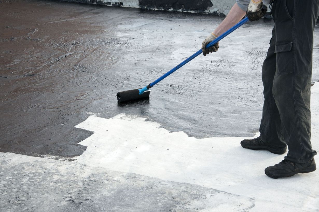 Person applies black sealant with a roller to a white surface outdoors.