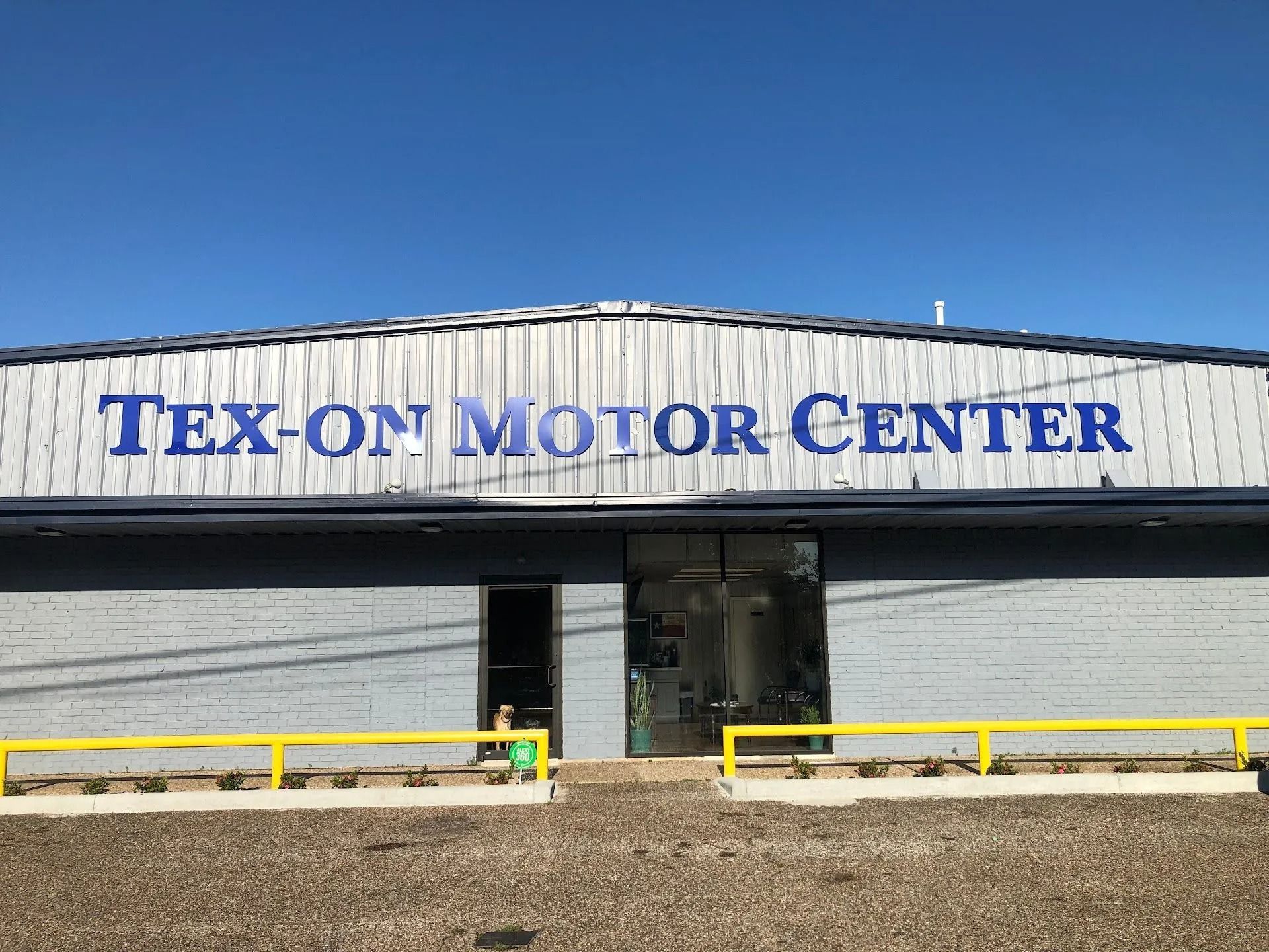 Tex-On Motor Center storefront with blue sign and yellow safety rails under a clear sky
