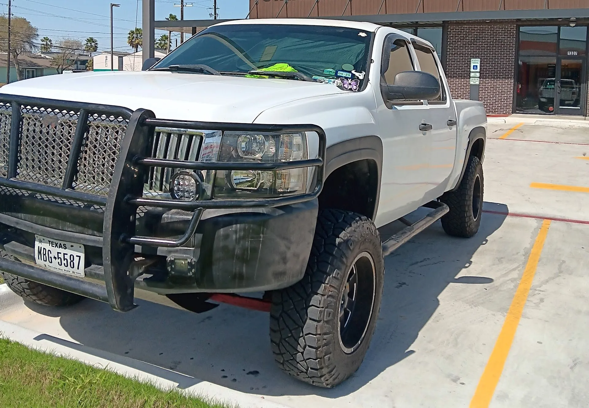 White lifted pickup truck with black grille guard parked in a lot under bright sunlight