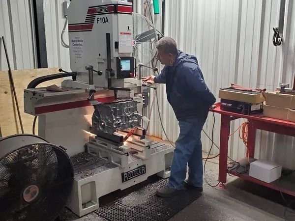 Worker operating a vertical band saw in a workshop, cutting metal on a cluttered workbench.