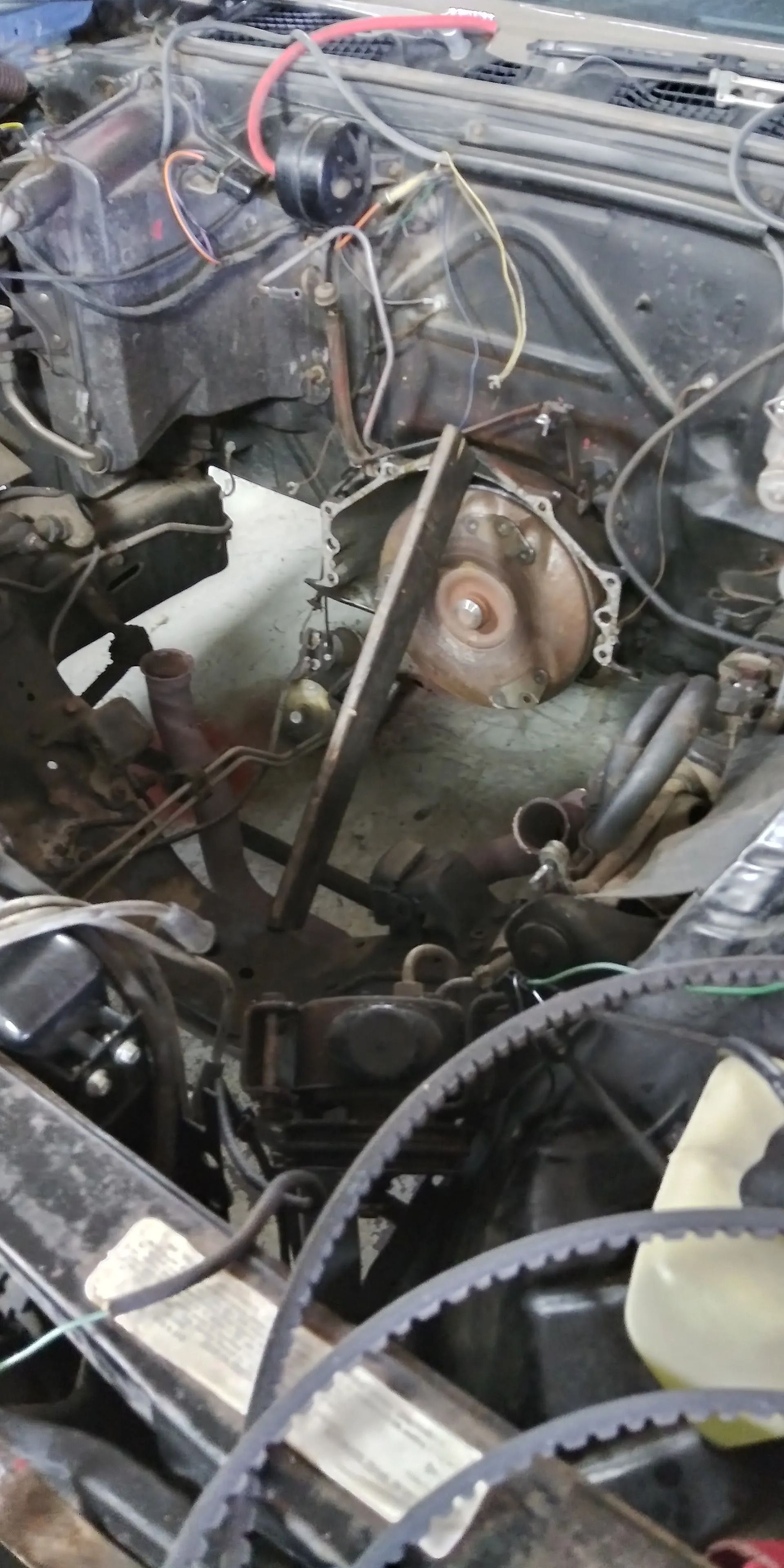 Close-up of a car engine bay with exposed wires, hoses, and a rusty engine component.