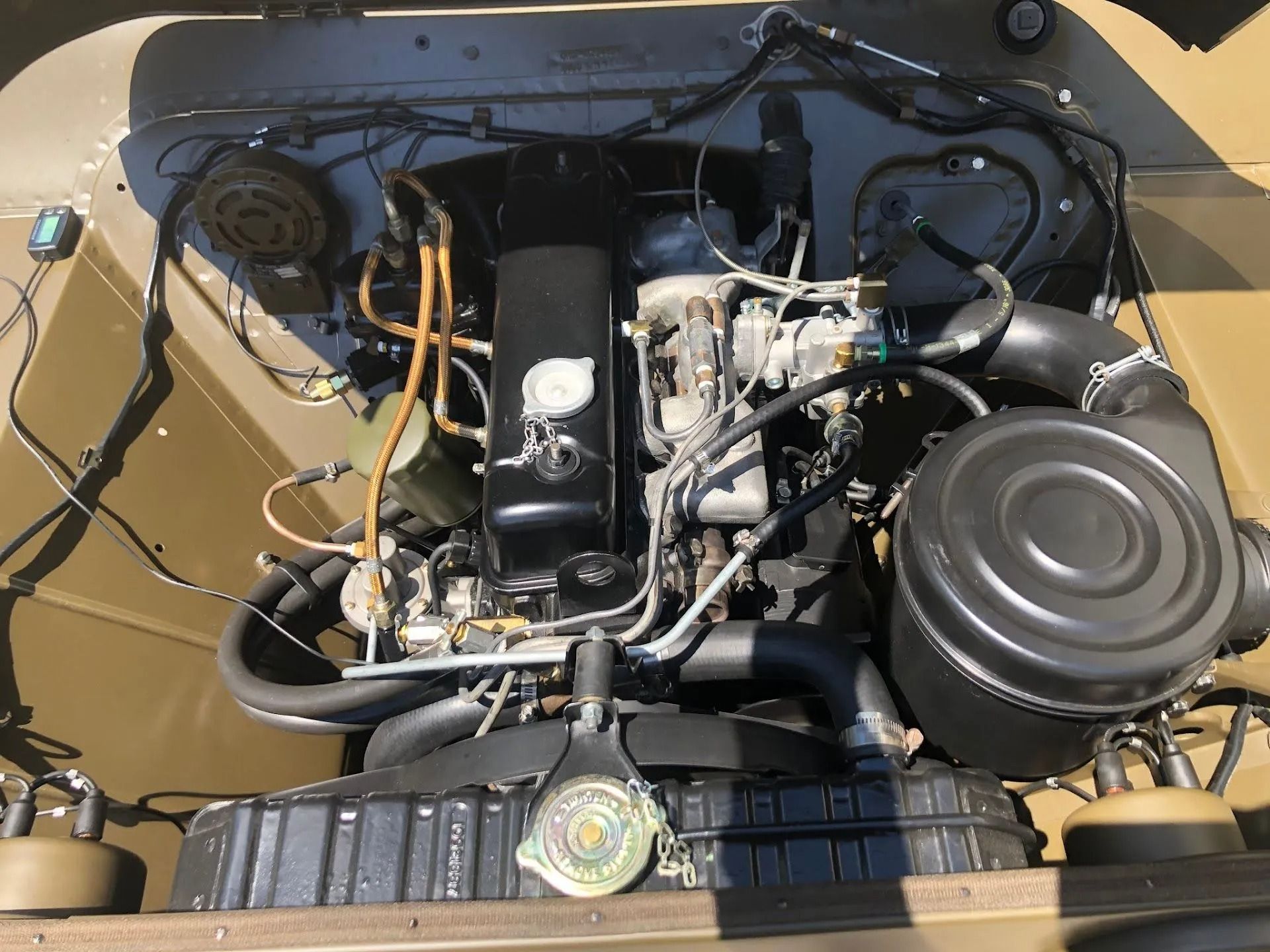 Open car engine bay with black and chrome components on a tan body.